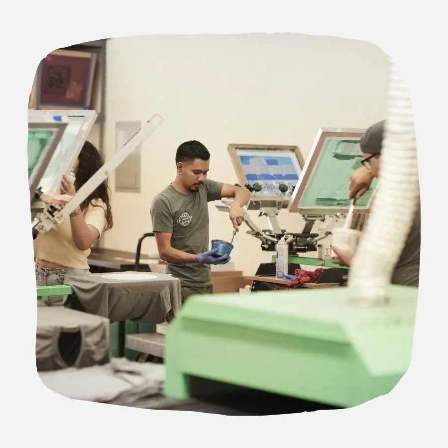 Workers operating screen printing machinery in a busy workshop setting.