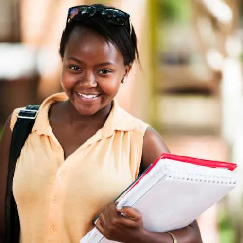 Confident young female student carrying documents and smiling.