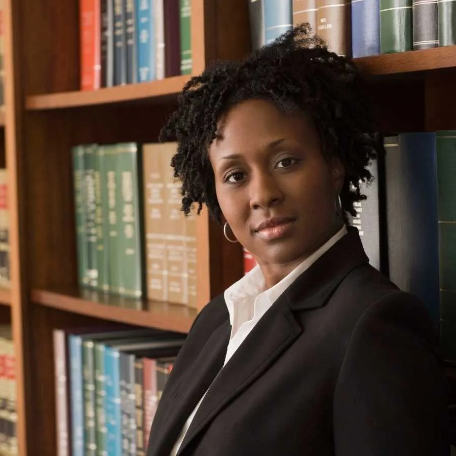 A professional Black female attorney stands confidently in a law library.