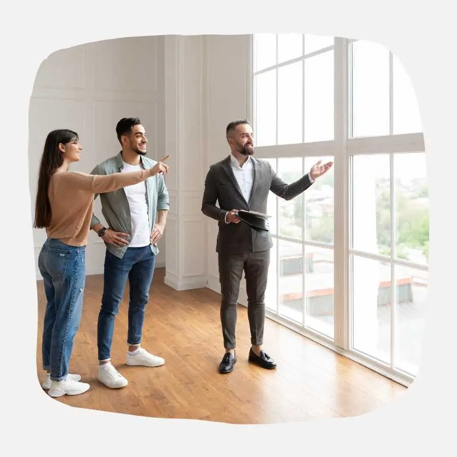 Real estate agent showing a bright, spacious room to a young couple, symbolizing future homeownership.