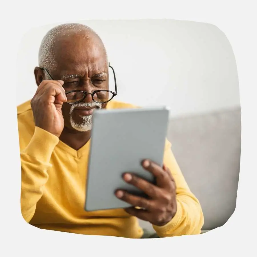 Elderly man with glasses intently reading on a tablet, engaging with digital content.