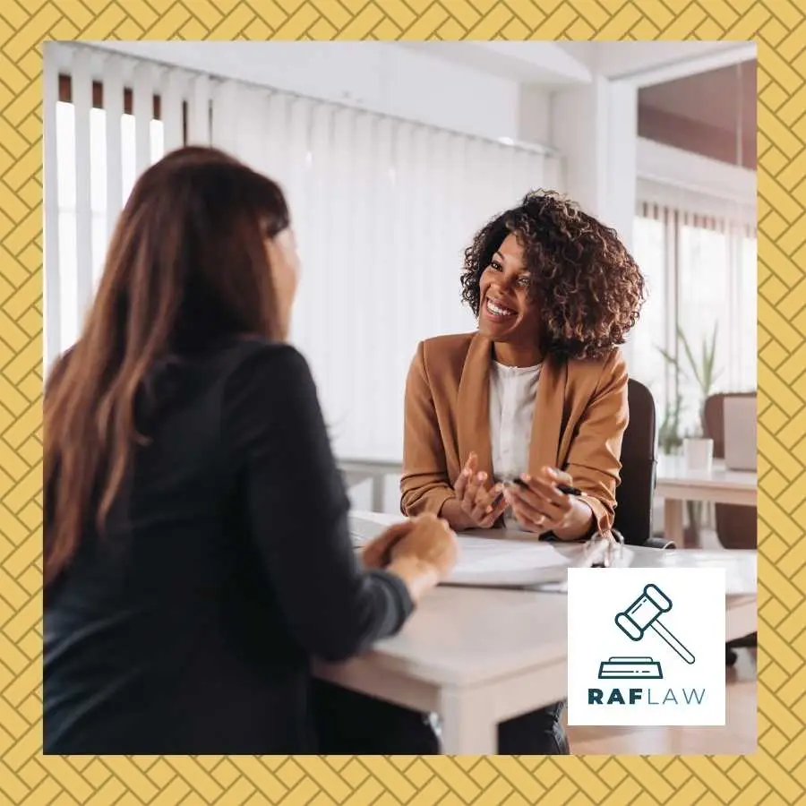 Two professional women in a friendly discussion across a desk with the RAF LAW logo