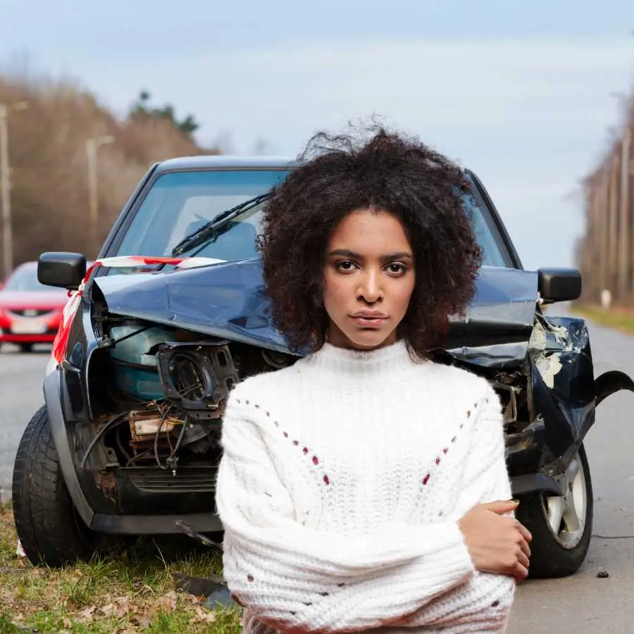 Woman standing confidently in front of a damaged car on a roadside