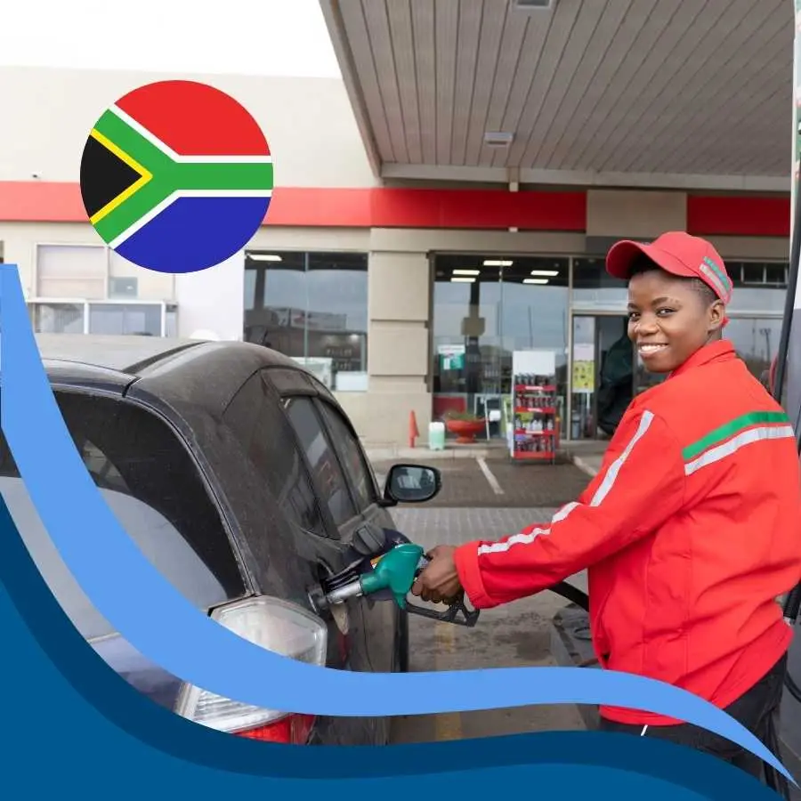 A smiling service station attendant in South Africa refueling a car with a backdrop of the South African flag.