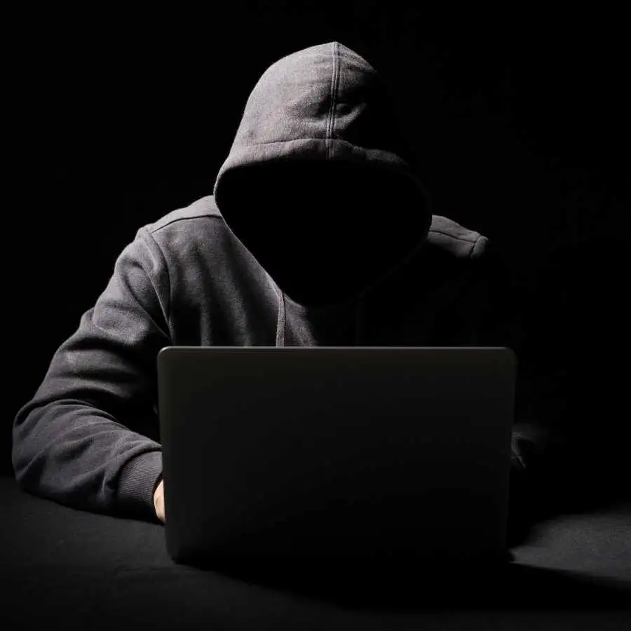 Person in a hoodie using a laptop in a dark environment