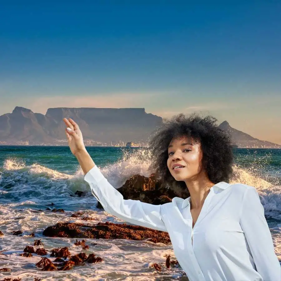 Woman gesturing towards the Table Mountain from the rocky shoreline