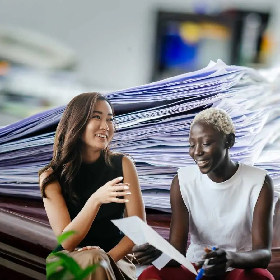 Two women smiling and discussing documents being collected