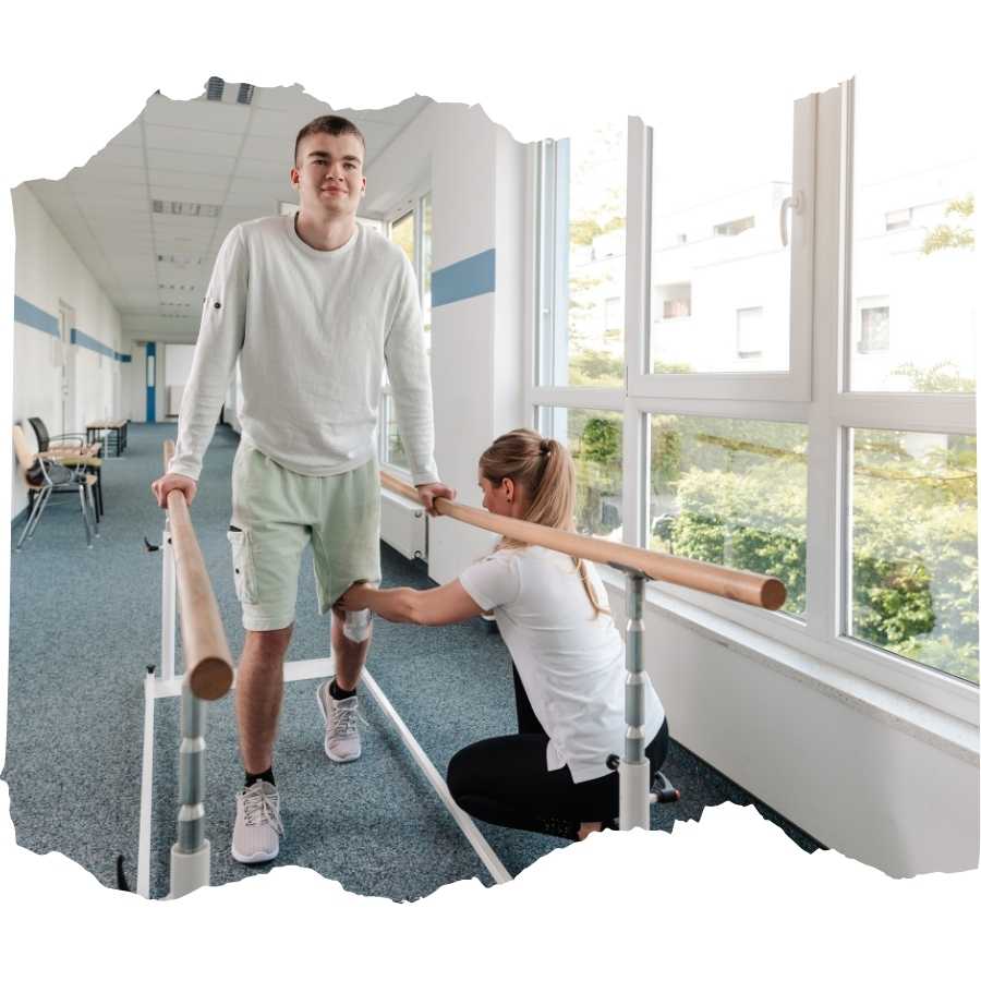 Young man using parallel bars for rehabilitation with assistance from a therapist