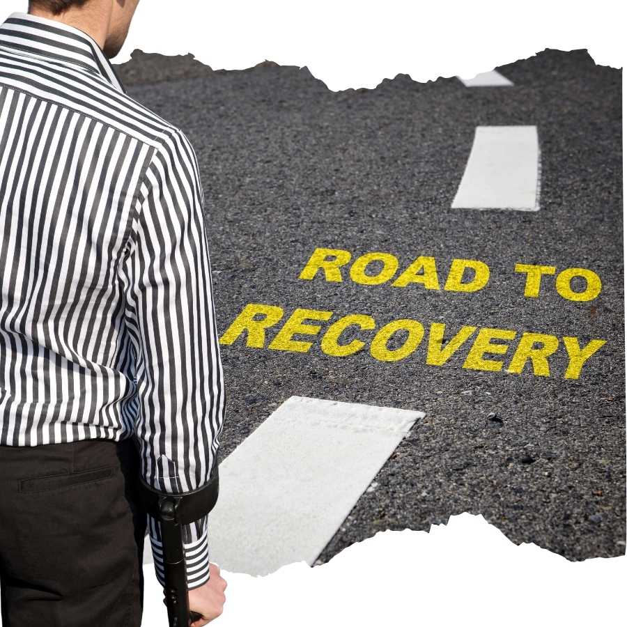 Man with a crutch standing at the start of a road marked "ROAD TO RECOVERY"