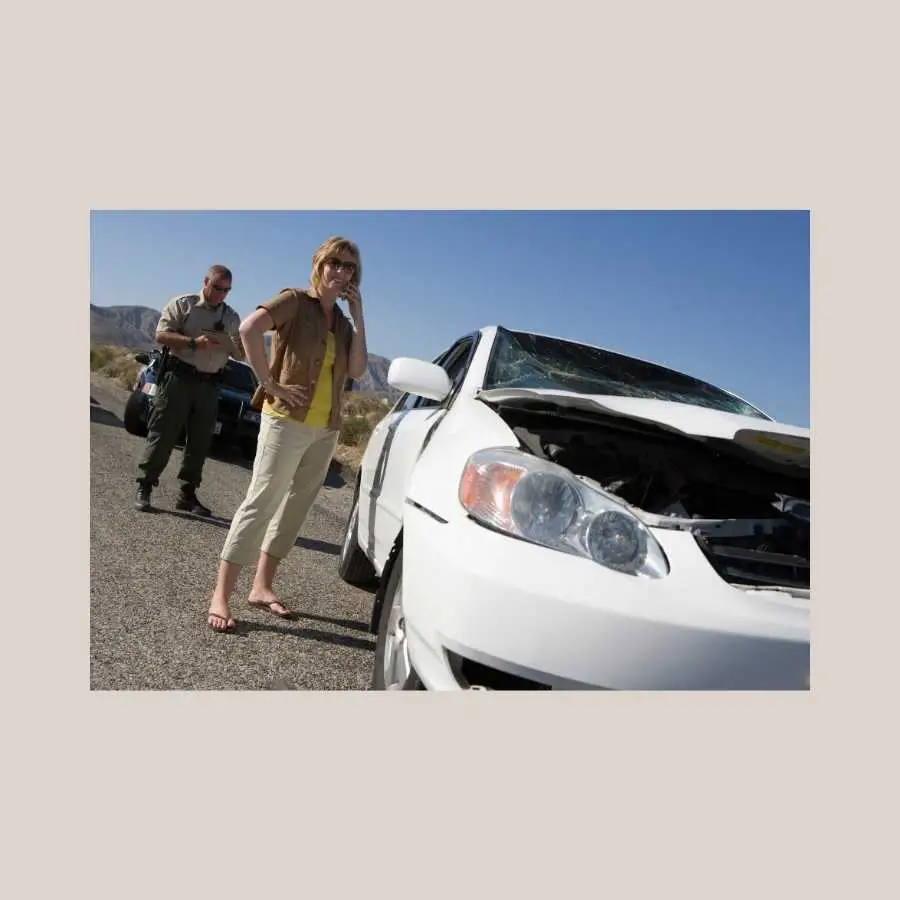 Woman on phone standing by a damaged car with a police officer in the background