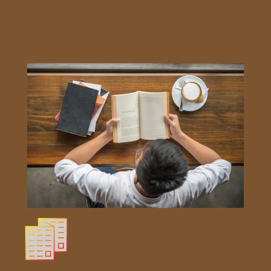 Person reading a book at a wooden table with a cup of coffee educating themselves on the various aspects of medical assessments.