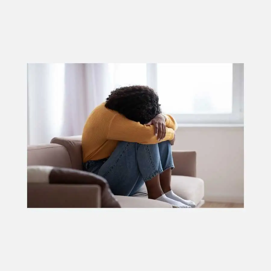 Woman distressed and sitting on couch, covering face with arms