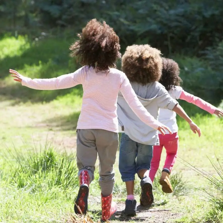 Three children running outdoors on a grassy path, enjoying nature