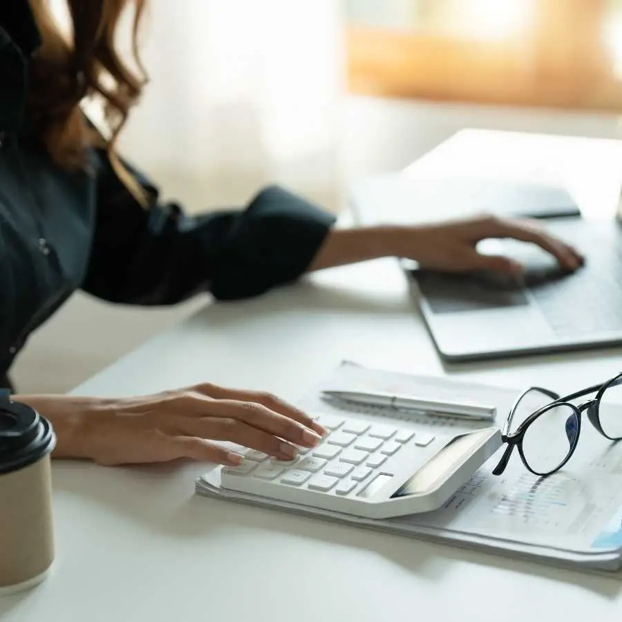 Woman calculating finances on calculator with laptop and documents on desk